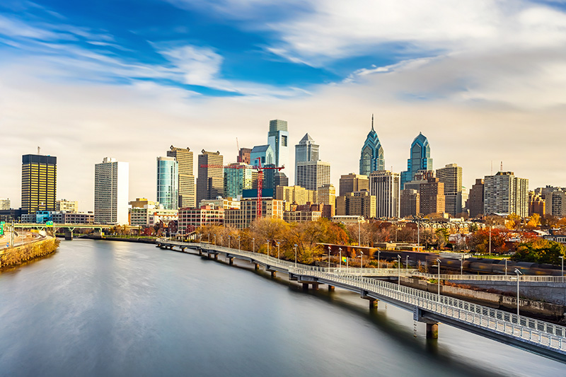The image is a photograph of an urban skyline with the city s skyscrapers and a river, taken from a high vantage point looking towards the downtown area.